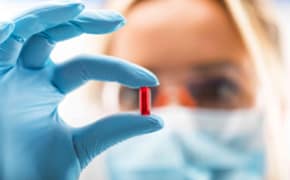 The image depicts a scientist closely examining a pharmacology drug while wearing blue gloves. Their focused attention suggests a laboratory setting, where precision and care are essential.