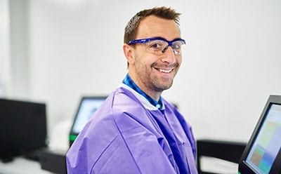 A man working in the biosafety lab  wearing personal protective equipment looking and smiling at the camera.