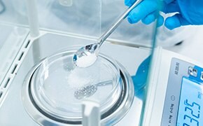 A scientist wearing blue gloves is measuring a white powder on a digital scale, representing PEGs (polyethylene glycols) and PEOs (polyethylene oxides) used in various scientific and industrial applications.