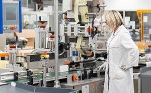 Woman in a labcoat and goggles inspecting a lateral flow membrane manufacturing line.