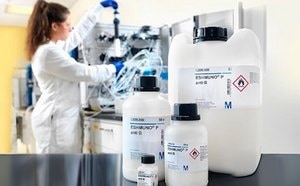 4 different sizes of Affinity chromatography with Eshmuno® resin bottles sit on a black counter with a scientist working on a piece of machinery in the background