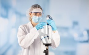 Large, brown solvent bottle with Supelco® branded label is opened by a lab worker wearing blue nitrile gloves. Only the hands and lower arms of the worker are shown. One small brown solvent bottle and two small white bottles can be seen in the background.