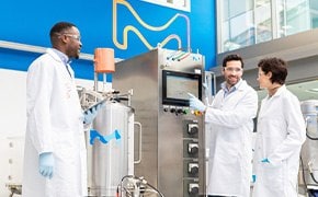 Three scientists stand next to a bioreactor.