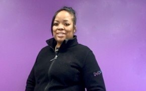 Chevon Adams wears a black fleece and stands in front of a purple wall. 