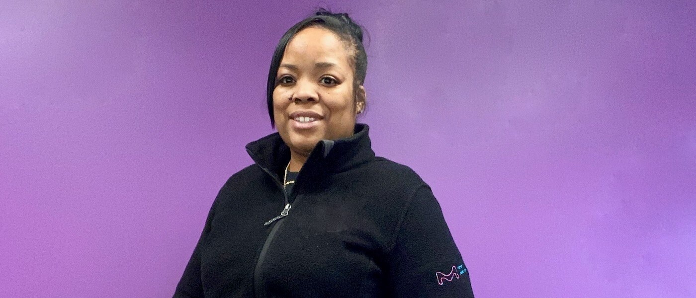 Chevon Adams wears a black fleece and stands in front of a purple wall. 