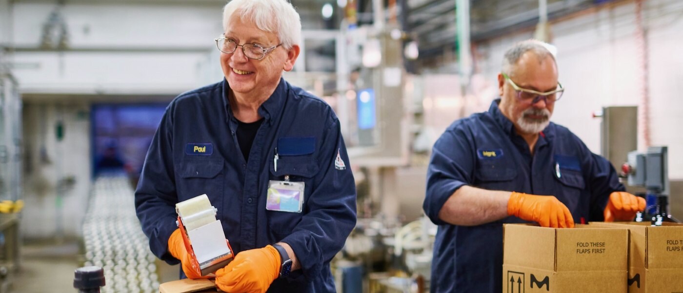 Two employees wear uniforms, gloves and safety glasses and package boxes. 