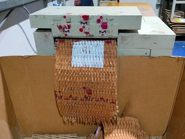 A tan machine shows a shredded box emerging. Below several other shredded boxes are visible.  