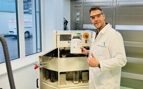 Thomas Kipping wears safety glasses and a lab coat standing next to a laser 3D printer.