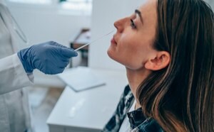 A clinician wears blue gloves and inserts a nasal swab into a woman’s nostril, who is leaning back