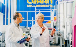 Two researchers wear safety glasses and stand next to large bioreactors