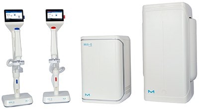 Two medical devices on stands with screens, one red and one blue, alongside a compact white unit and a larger white box. All devices feature the M logo.