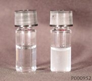 Two small glass vials on a neutral background. The vial on the left contains a clear liquid, while the vial on the right holds a cloudy, white liquid, both sealed with silver caps.